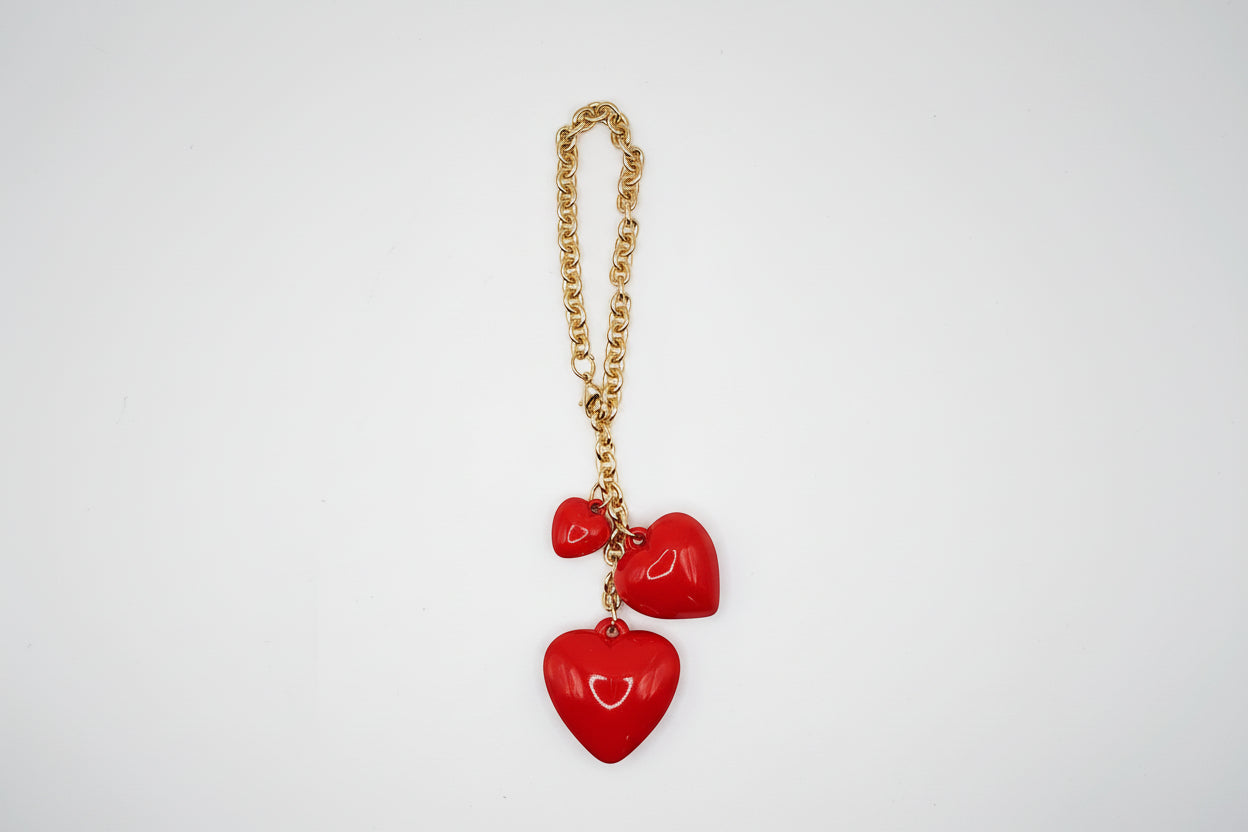 Gold chain with red heart-shaped pendants on a light gray background