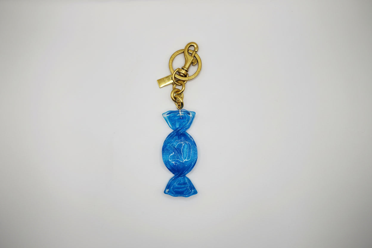 Blue candy-shaped keychain with gold chain on a light gray background