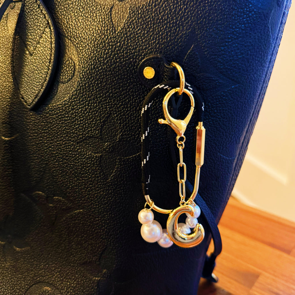 Gold keychain with pearls attached to a black textured surface