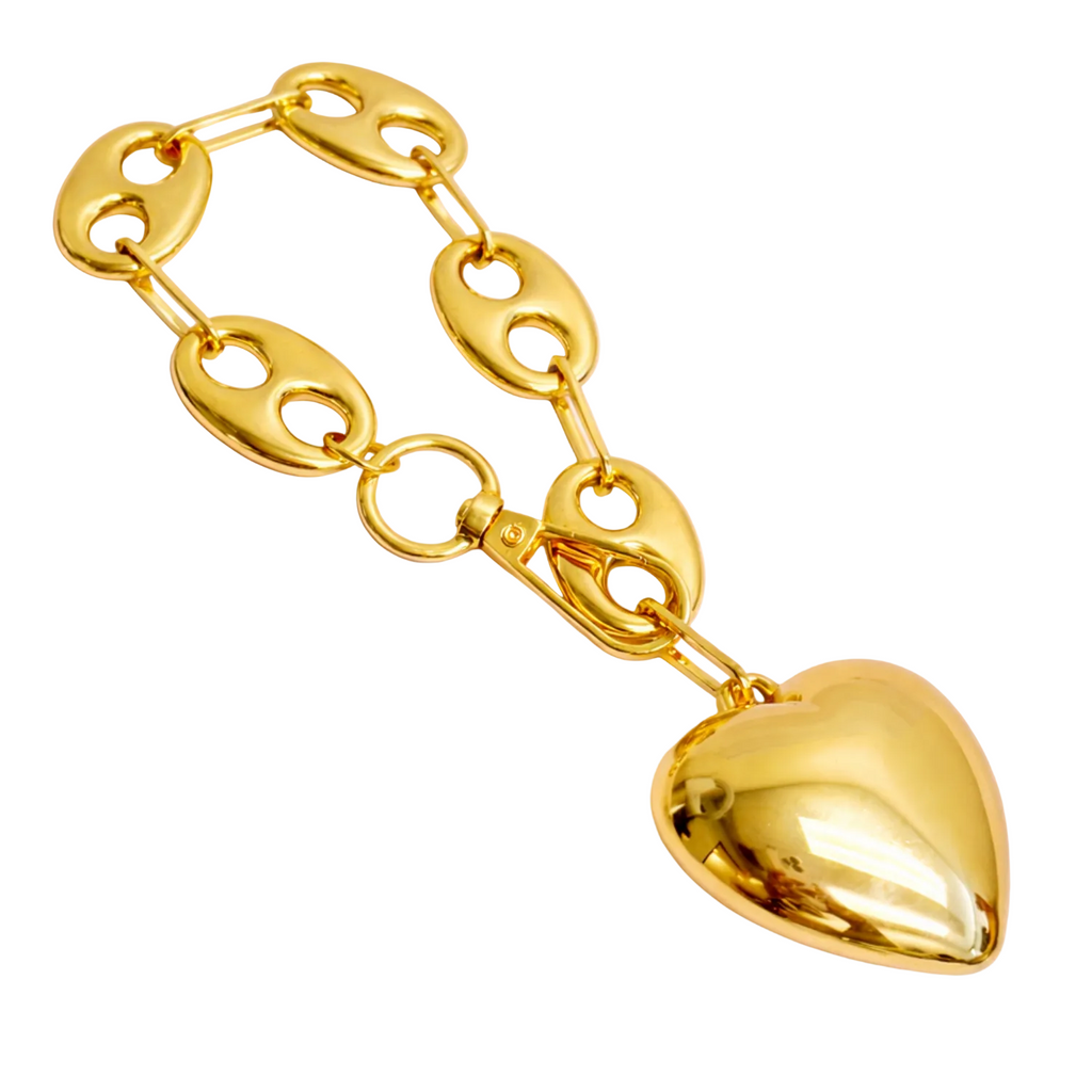 Gold chain bracelet with a heart-shaped pendant on a light pink background