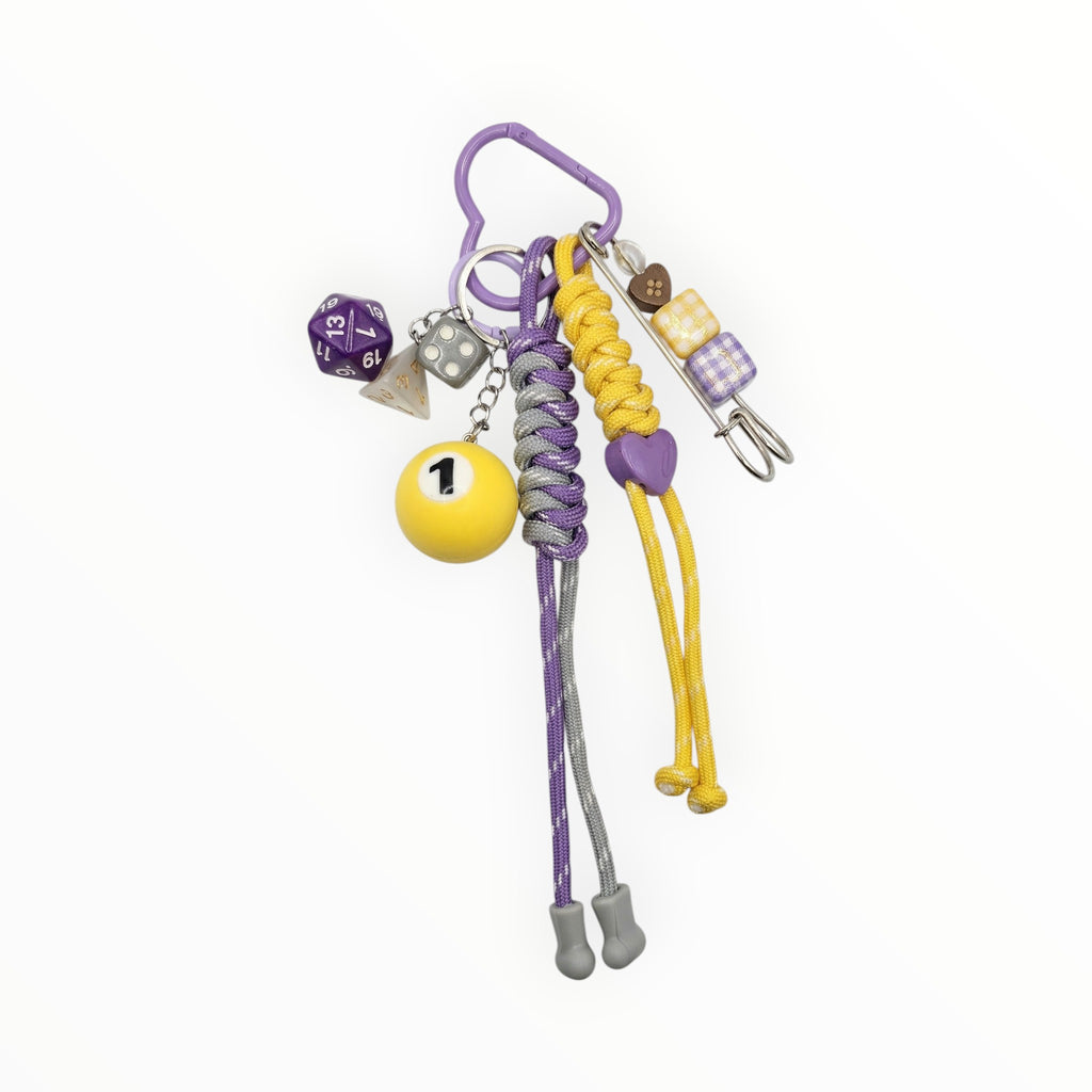 Game Night Maximalist Paracord Bag Charm with yellow and purple paracord, dice cluster, 1 pool ball, safety pin, heart clip