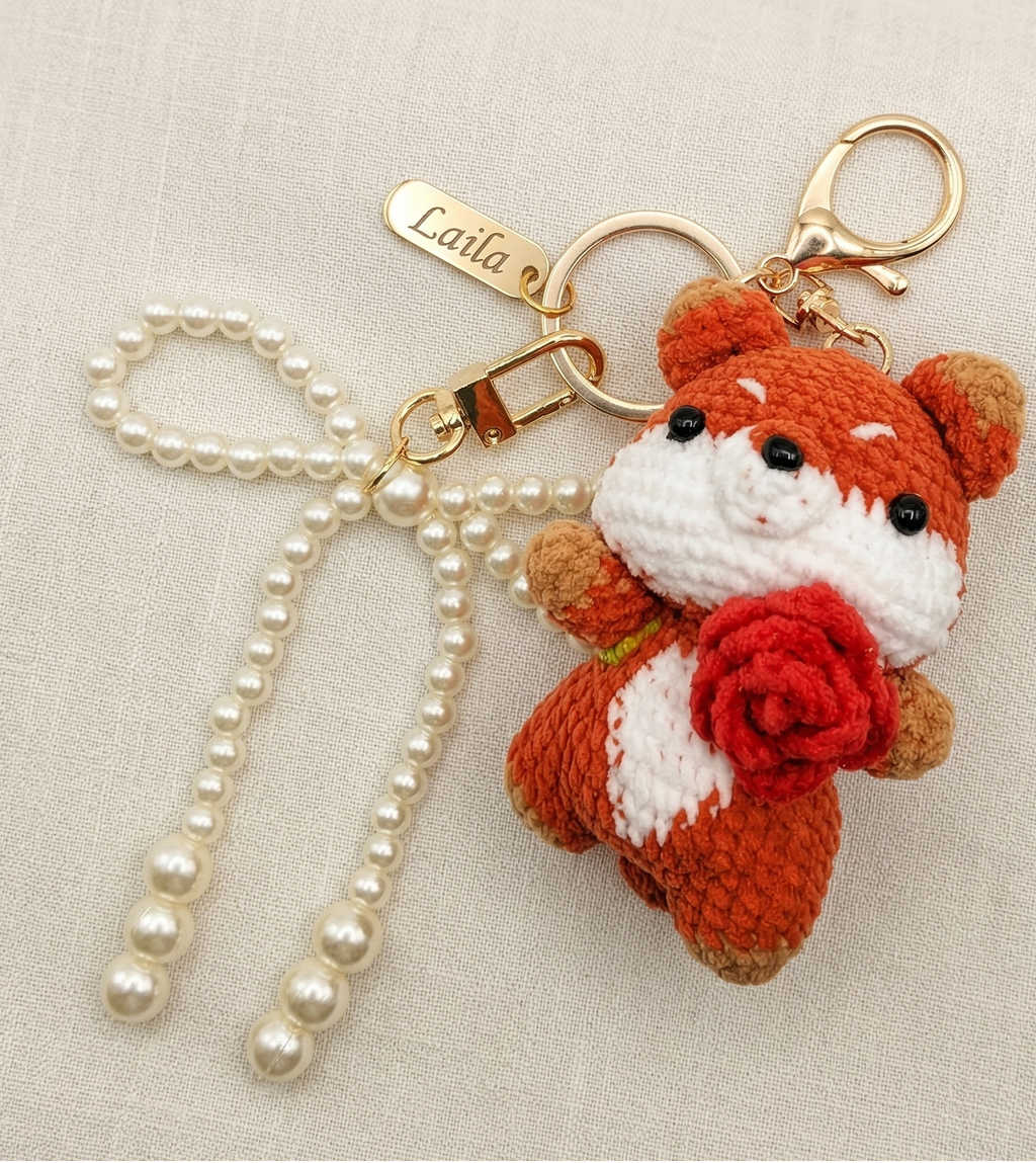 Crocheted fox keychain with pearl ribbon on a beige background