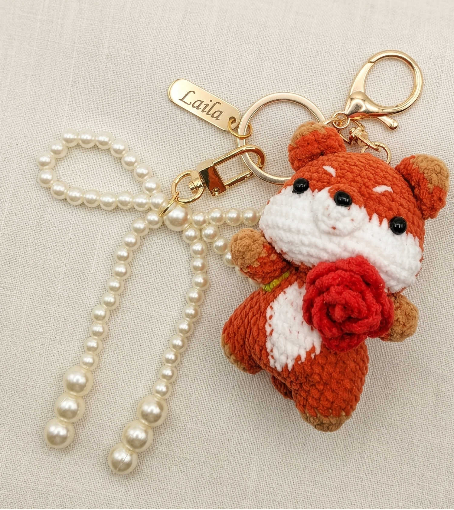 Crocheted fox keychain with pearl ribbon on a beige background