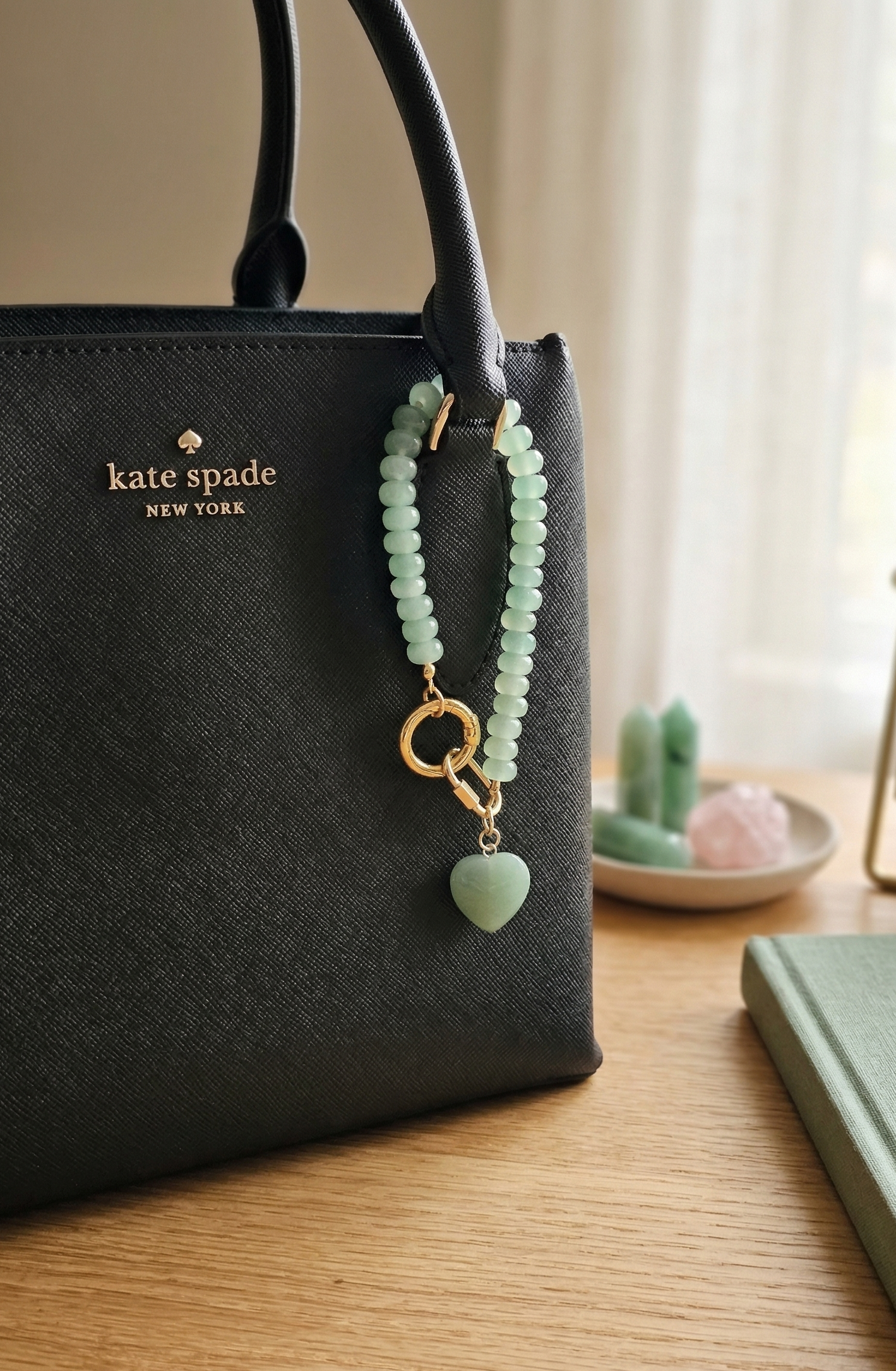 Black Kate Spade handbag with a green beaded charm on a wooden surface.